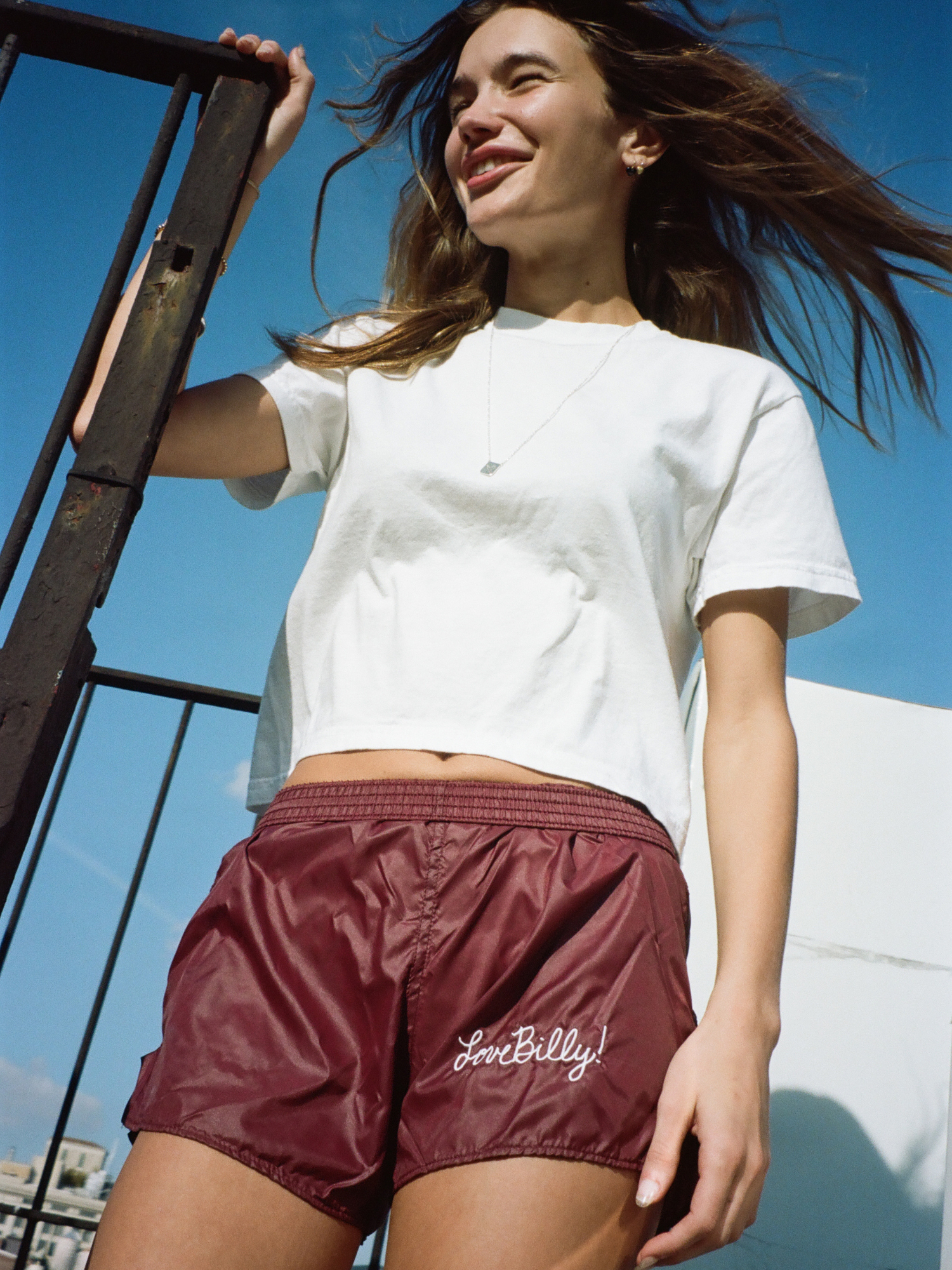 Young girl smiling with burgundy shorts and silver tag necklace by love billy on.