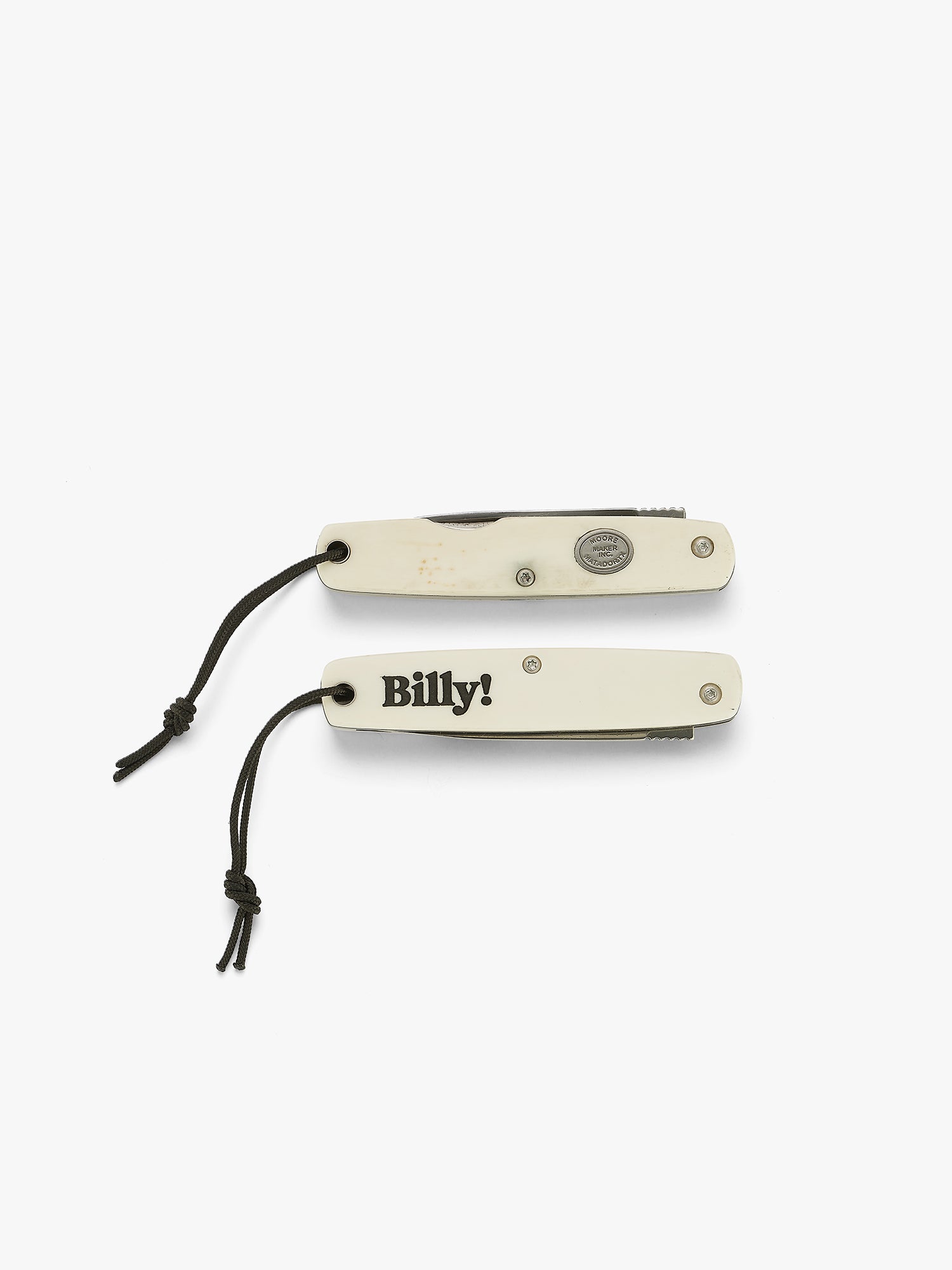 Two closed white pocket knives with black 'Billy!' engraving. Made in partnership with moore maker, inc in matador, texas.