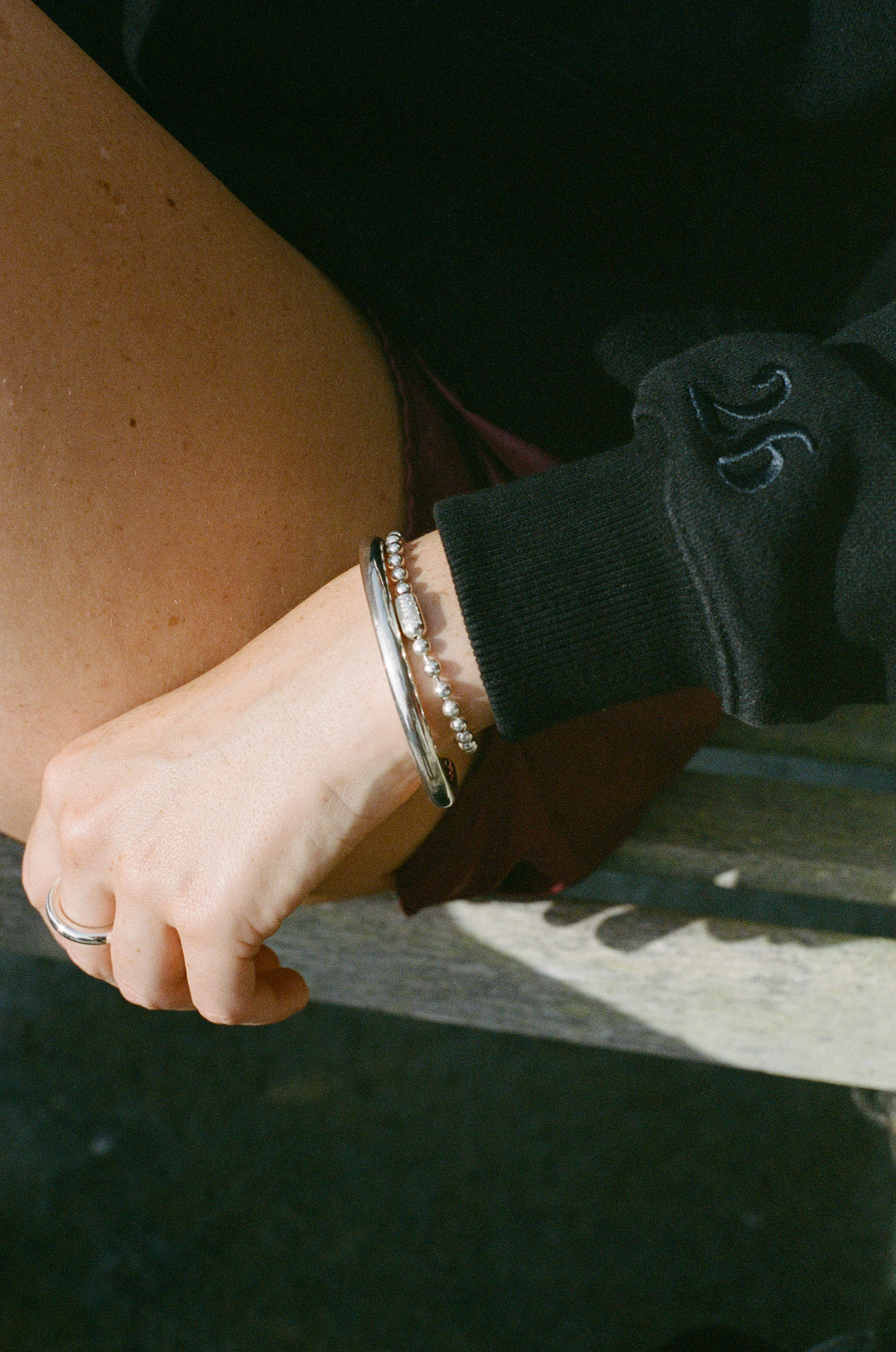 Close-up of a person's wrist with a carousel bracelet, a ball chain bracelet and a silver carousel ring. Showing wearing a black sleeve embroidered with a "26".