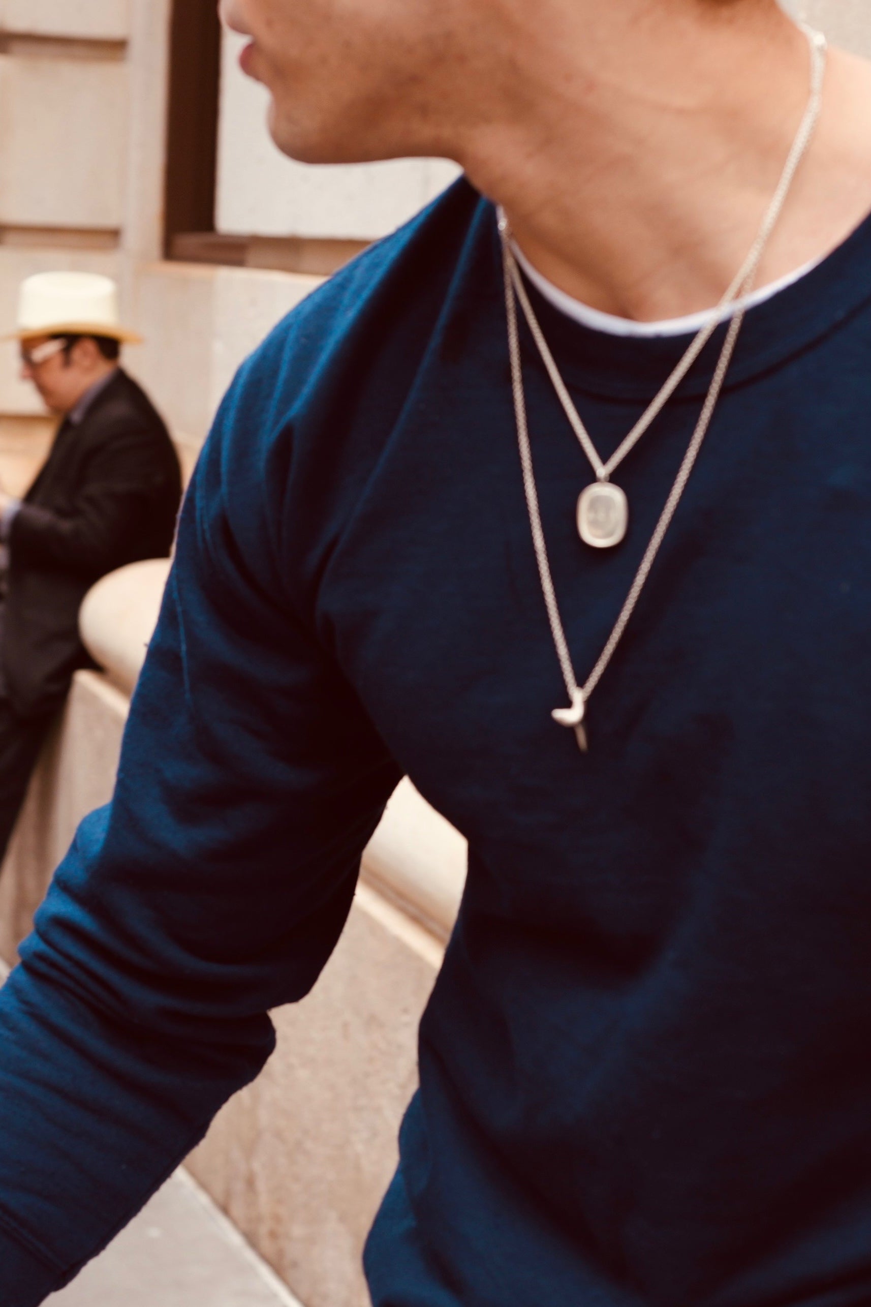 Person wearing a blue shirt and layered necklaces with a blurred background