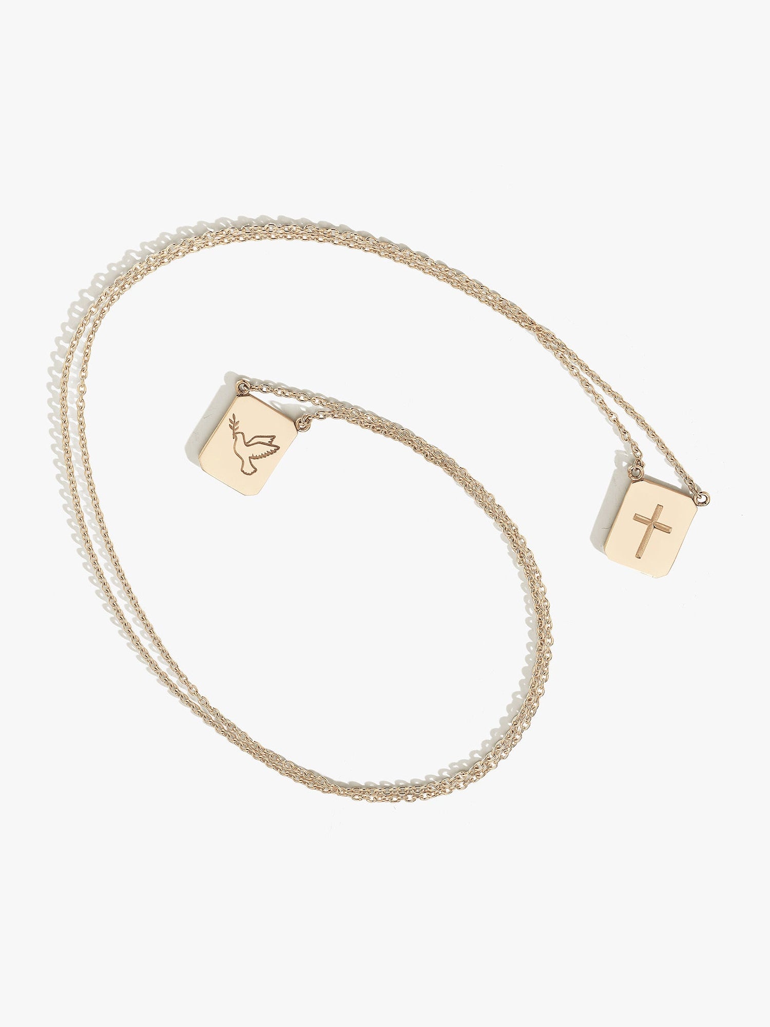 Gold necklace with two pendants on a white background. one pendant has a cross, the other has a dove