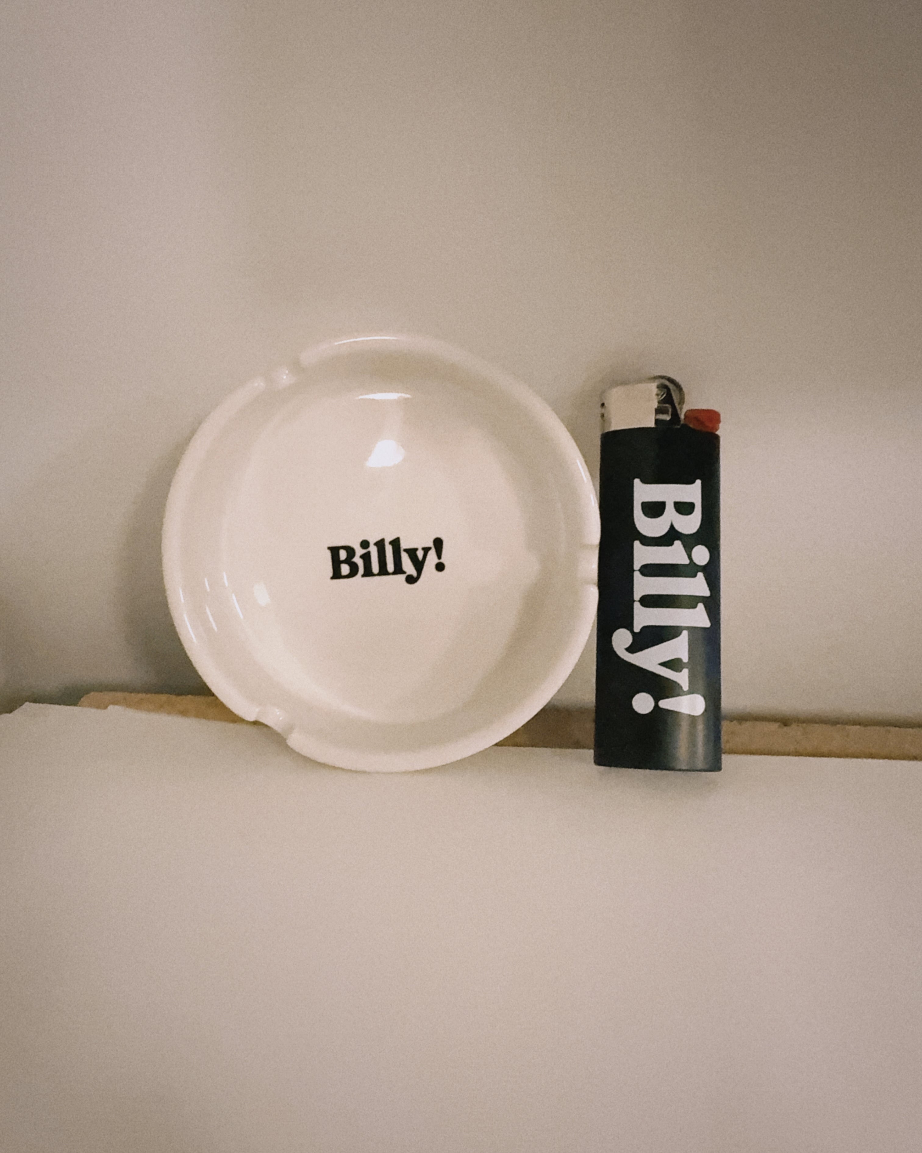White plate and black lighter with 'Billy!' text on a neutral background