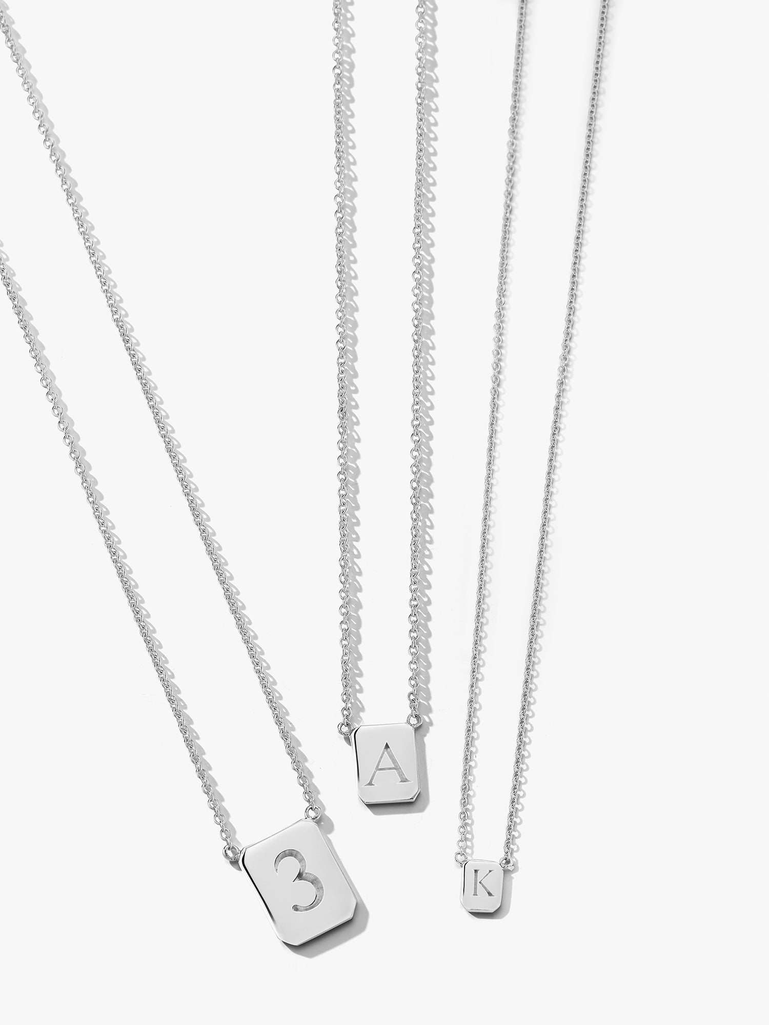 Three silver tag necklaces with rectangle pendants displaying custom monogrammed numbers and letters by love billy
