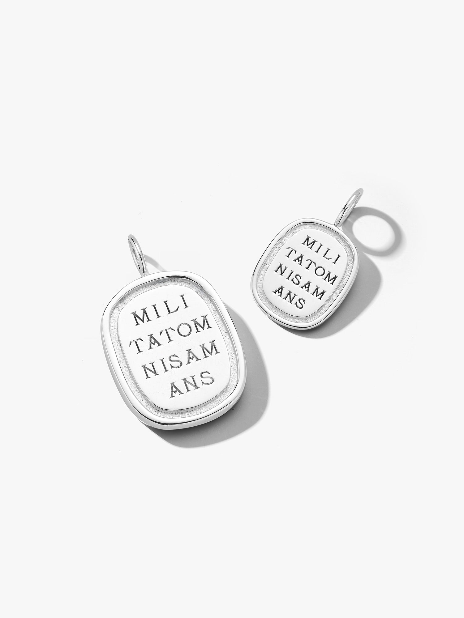Two silver love billy pendants with engraved text on a white background. Engraving reads "militatomnisamans" which translates loosely to "every lover is a solider"