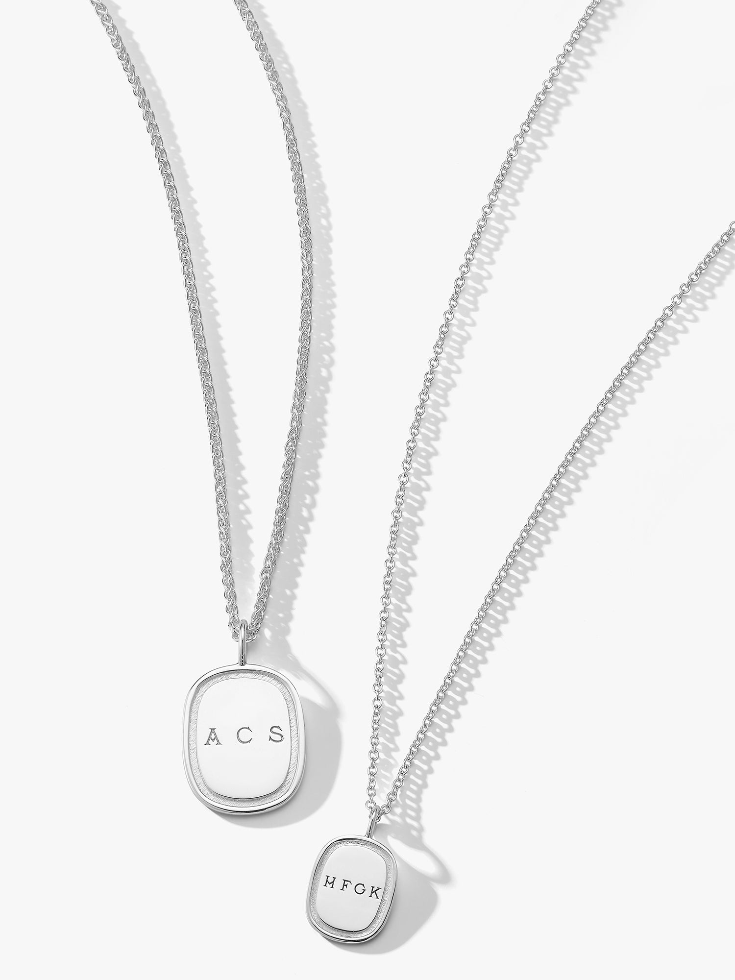 2 silver monogrammed oblong pendants by Love Billy next to each other, one on a wheat chain and other on a cable chain.
