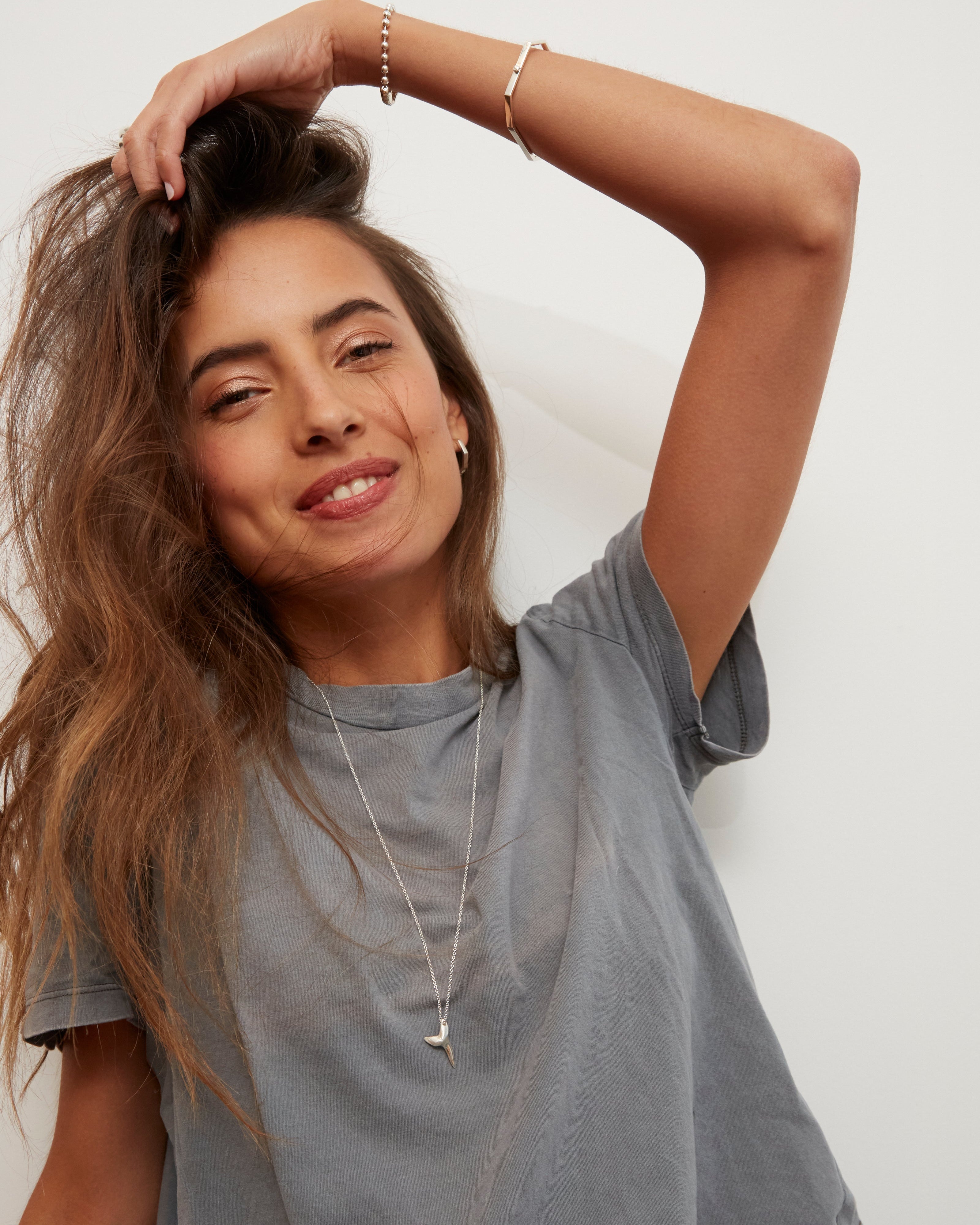 Woman wearing a gray t-shirt against a white background wearing a silver love billy shark tooth necklace