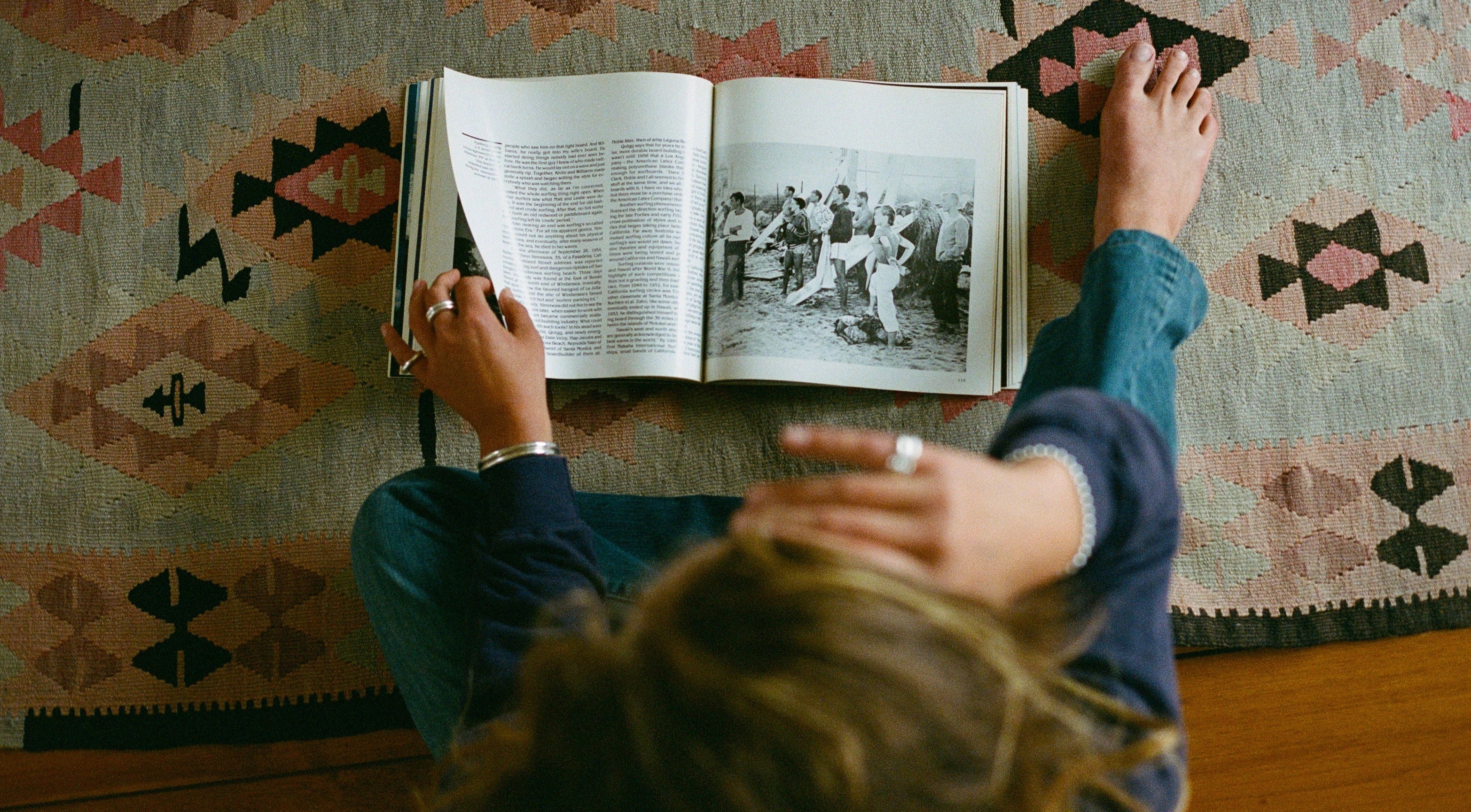 girl reading an open book with black and white photos on a patterned rug. 