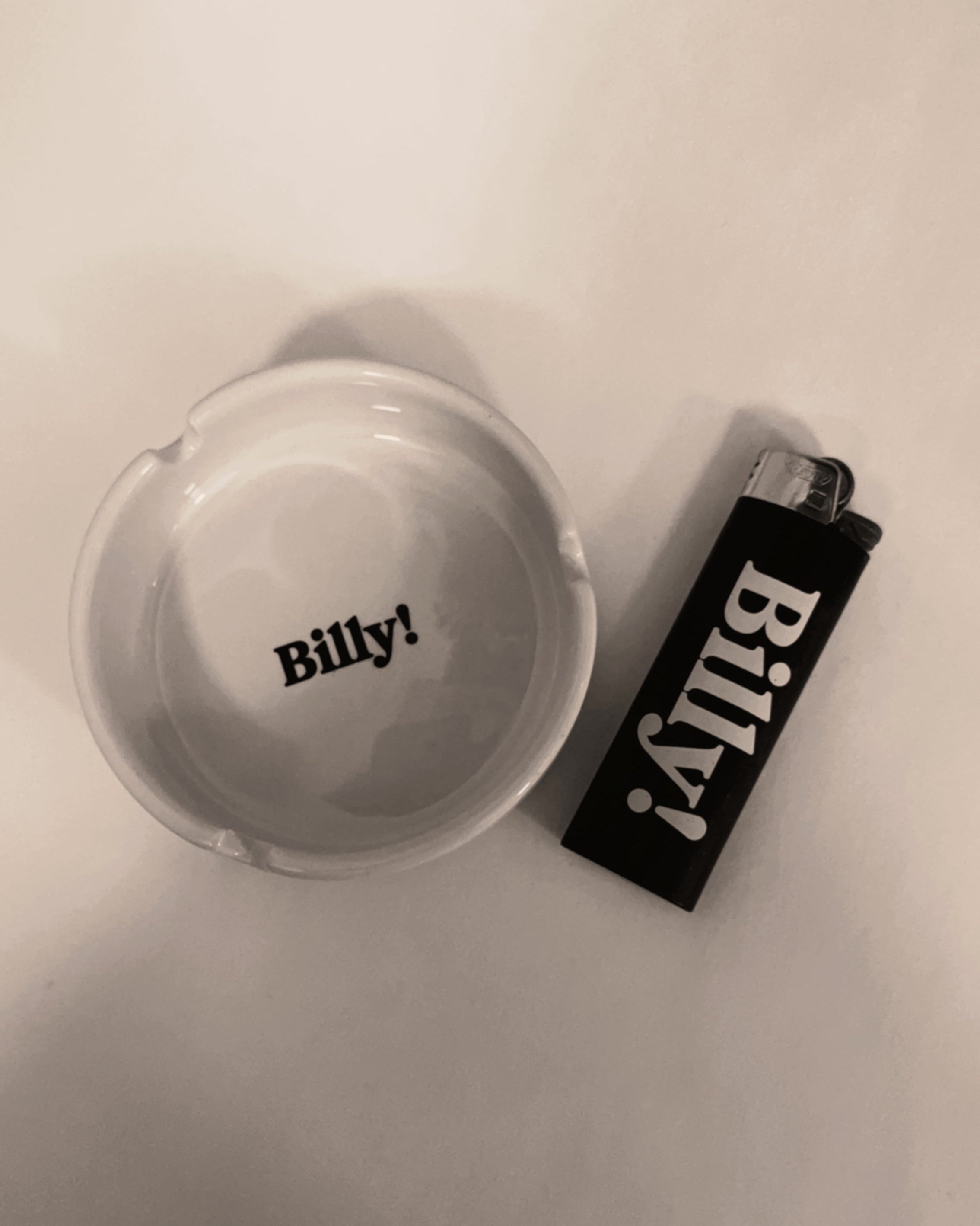 White ashtray and black lighter with 'Billy!' branding on a white surface.
