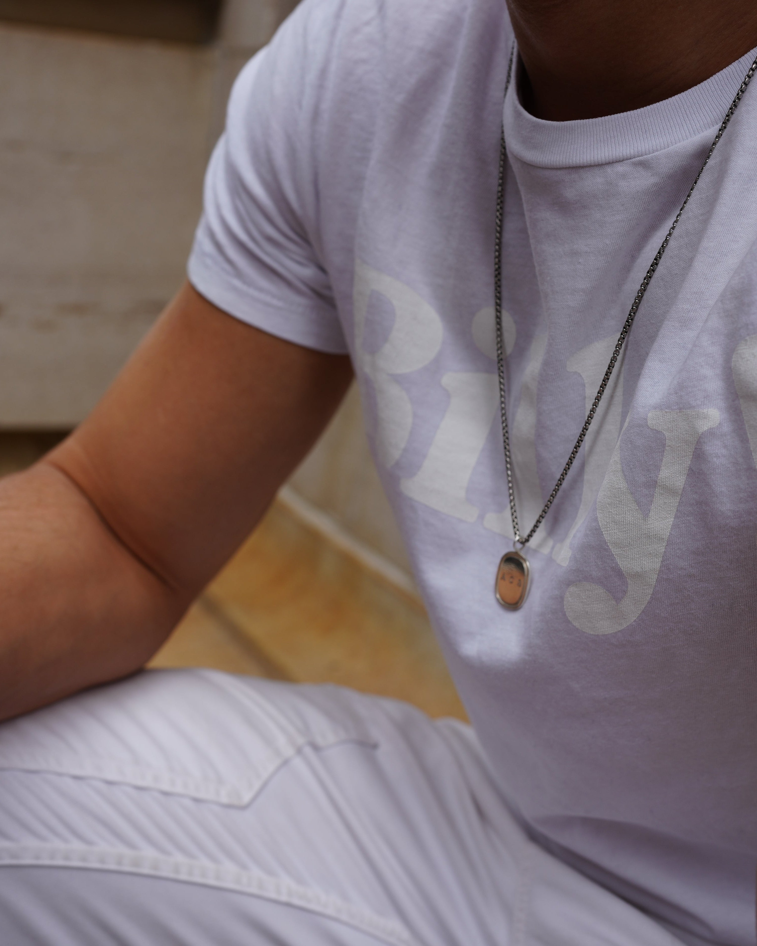 large silver oblong pendant by love billy, on a man sitting on bench