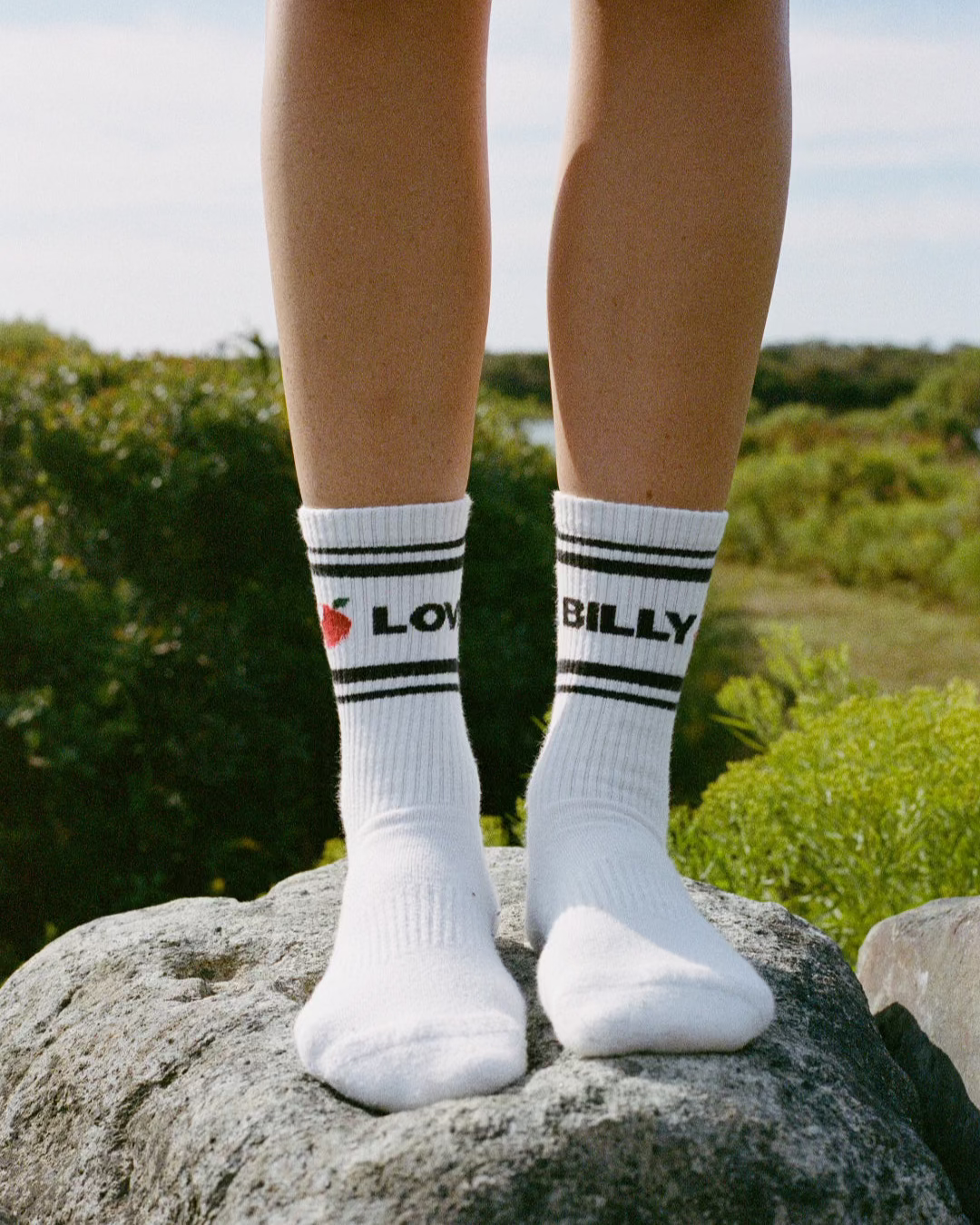 love billy tube socks on feet standing on a rock with an outdoor background. classic tube socks. a good new york city souvenir that you won't find on canal street.