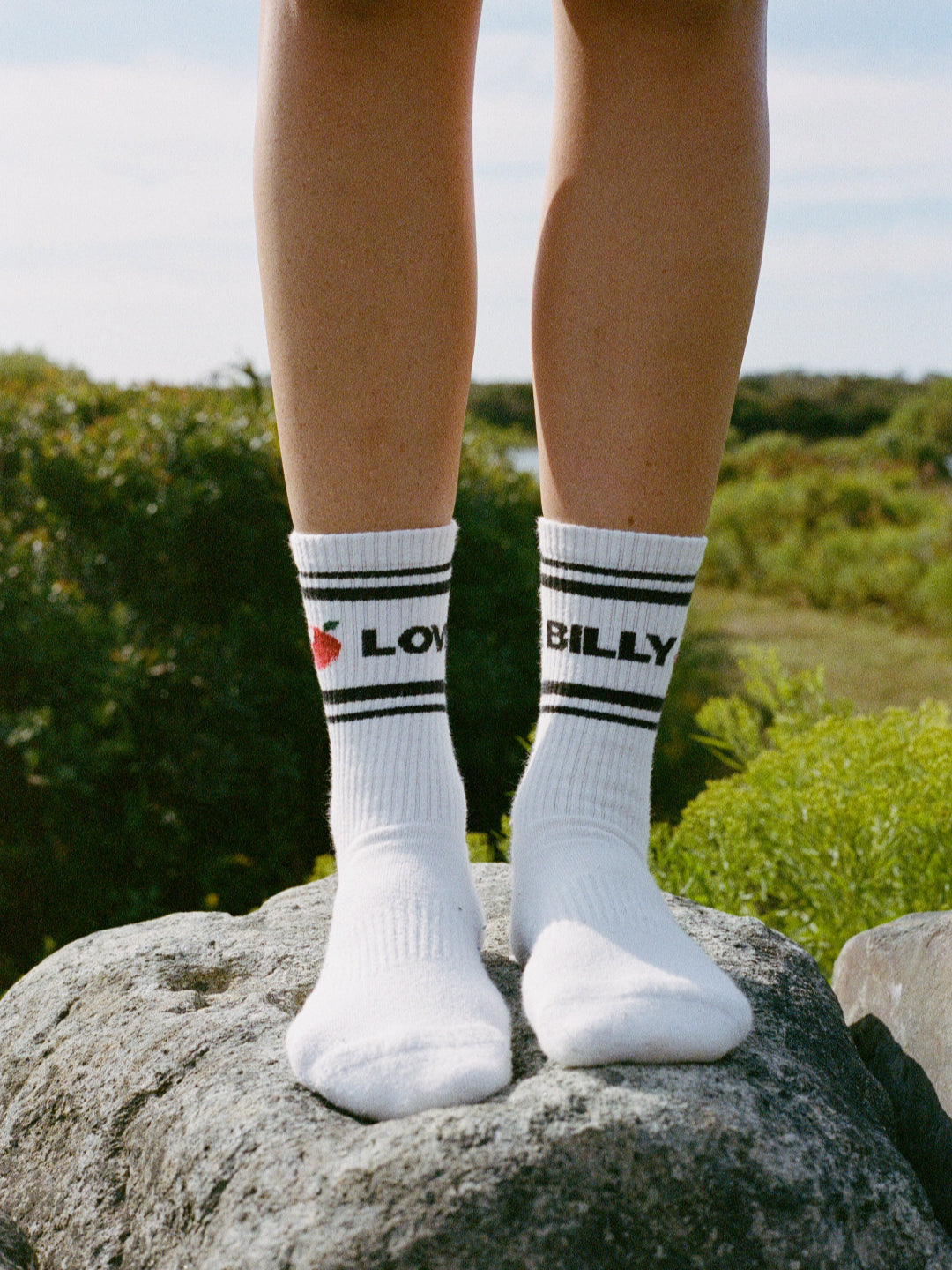love billy tube socks on feet standing on a rock with an outdoor background. classic tube socks. a good new york city souvenir that you won't find on canal street.