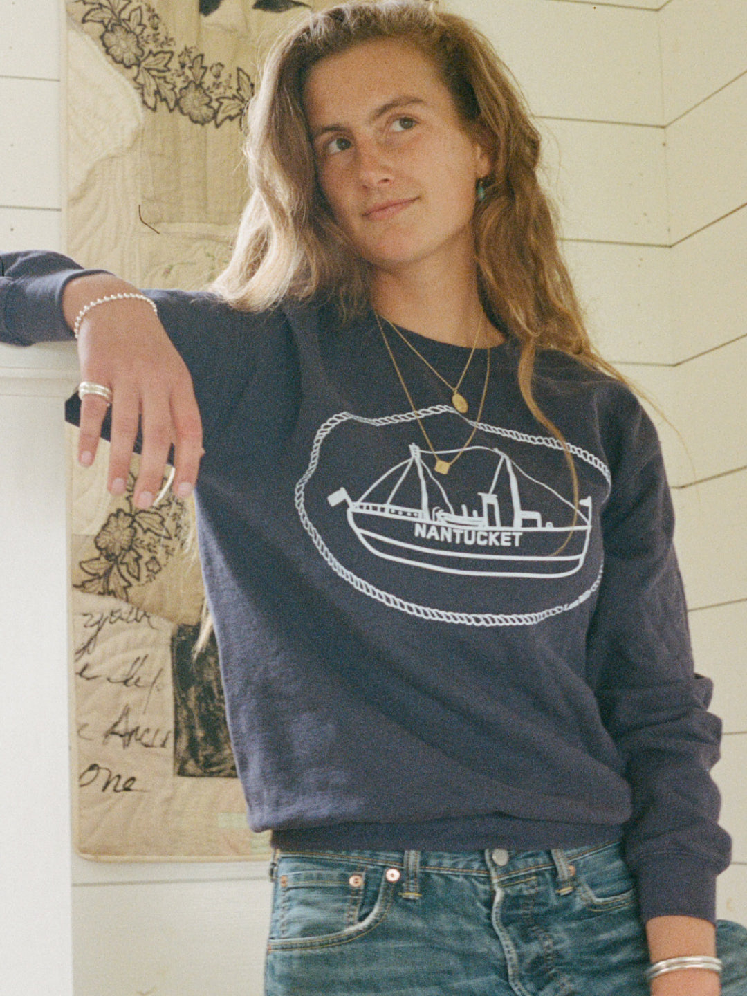 red head wearing a love billy sweatshirt with hand drawn nantucket lightship boat design, leaning on staircase